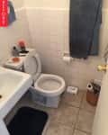 Small bathroom with white tiles, toilet, sink, blue towel, and toiletries on the tank.