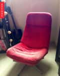 Red lounge chair with metal legs in a room with a guitar and bookshelves.