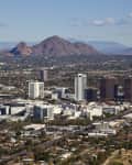Cityscape of Phoenix with tall buildings and Camelback Mountain in the background.