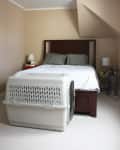 Bedroom with a wooden bed, gray pillows, white bedding, and a large pet crate in the foreground.
