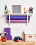 Home gym setup with yoga mats, kettlebell, sneakers, and motivational sign on a shelf.