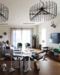 Modern living room with geometric chandeliers, gray sofa, green chairs, wall art, and a large TV.