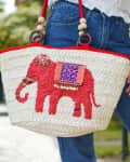 Woven straw bag with red elephant design, held by person in jeans and white top.