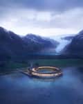 Circular building on a lake surrounded by mountains and a glacier under a cloudy sky.