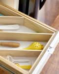 Open kitchen drawer with wooden dividers holding utensils, including a yellow whisk, wooden spatula, and citrus juicer.