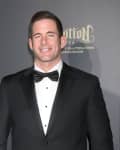 Man in a black tuxedo with a bow tie smiling at a formal event backdrop.