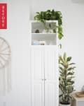 White cabinet with plants on top and beside it, macrame wall hanging, and wooden floor.