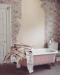 Pink clawfoot bathtub with torn floral wallpaper piled on top, in a vintage bathroom.