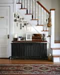 Staircase with white spindles, wall decor, radiator, and a console table with books, mugs, and framed photo.
