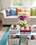 Colorful living room with a white sofa, vibrant pillows, glass coffee table, and decorative items like flowers and candles.