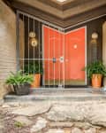 Orange double doors with metal gate, flanked by potted ferns, brick walls, and house number 501.