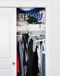 Open closet with clothes on hangers, shelves with folded linens, and a lamp nearby.