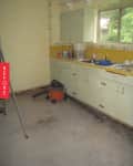 Old kitchen with yellow countertops, cluttered sink, cleaning supplies, and a vacuum cleaner on the floor.