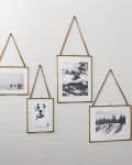Four black and white photos in brass frames with leather straps on a white brick wall.