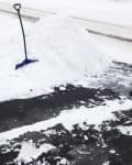 Snow shovel leaning against a pile of snow on a cleared driveway.