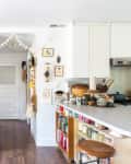 Cozy kitchen with wooden sideboard, potted plant, hanging decor, and open shelves with jars and kitchenware.