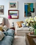 Living room with blue velvet sofa, cream armchair, abstract art, tulips, and decorative pillows on a fluffy rug.