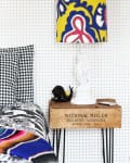 Colorful lamp with abstract pattern on a wooden crate table, next to a bed with houndstooth and multicolored bedding.