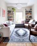 Cozy living room with white sofa, patterned rug, bookshelves, and a window seat with cushions.