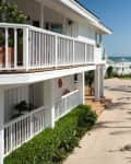 Beachfront house with white railings, palm trees, and ocean view along a sunny pathway.