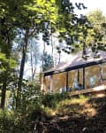 Modern cabin with large windows nestled in a forested hillside.
