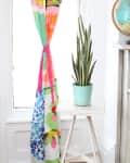 Colorful floral curtain tied back next to a potted snake plant on a white stool by a window.