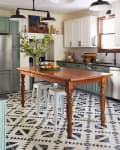 Kitchen with wooden island, metal stools, geometric tile floor, green cabinets, and black pendant lights.