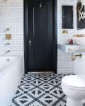 Black and white bathroom with geometric floor tiles, black door, white subway tiles, and gold fixtures.