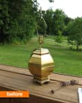 Brass lamp without shade on wooden deck, overlooking a green lawn and trees.