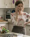 Woman in floral top talking on phone in a kitchen with plants, colorful towels, and baking items on the counter.