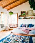 Cozy bedroom with wooden ceiling, colorful bedding, hanging crib, and decorative shelf above the bed.