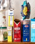 Assorted pantry items including baking soda, corn starch, rice, pasta, and cake flour on a wooden shelf.
