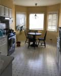 Yellow kitchen with white cabinets, black stove, round table, two black chairs, and a potted plant by the window.