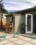 Small backyard studio with open French doors, two colorful chairs, potted plants, and a wooden potting bench.