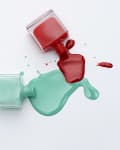 Spilled red and teal nail polish from two open bottles on a surface.