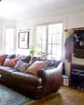 Living room with brown leather sofa, colorful pillows, teal ottoman, round coffee table, and large windows.