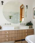 Modern bathroom with round mirror, double sinks, wooden vanity, white subway tiles, and a freestanding bathtub.