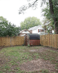 Fenced backyard with a small red shed, surrounded by trees and neighboring houses.