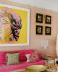 Pink living room with a bright yellow artwork, pink sofa, blue bar, and decorative pillows.