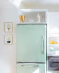 Mint green retro fridge in a bright kitchen with white cabinets, marble countertops, and a coffee maker.