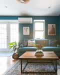 Living room with teal walls, a blue sofa, wooden coffee table, carved wall art, and French doors.