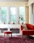 Two red armchairs, a saxophone, and potted plants in a sunlit room with large windows and a patterned rug.