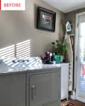 Laundry room with washer, dryer, ironing board, potted plant, and framed artwork on beige wall.