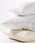 Stack of three fluffy white pillows on a light surface.