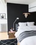 Modern bedroom with black accent wall, white bedding, gray throw, bull skull decor, and industrial lamps.