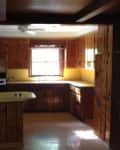 Wood-paneled kitchen with yellow countertops, a window above the sink, and a black stove.