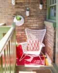 Small balcony with a white wicker chair, red patterned cushion, and wall-mounted planters on a brick wall.