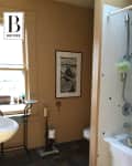 Bathroom with beige walls, framed artwork, pedestal sink, and tiled floor next to a bathtub with a showerhead.