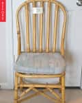 Bamboo chair with worn cushion and price tag, set against a white door.