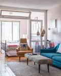 Living room with blue sofa, orange armchair, and a view into a bedroom with a metal bed frame and large windows.